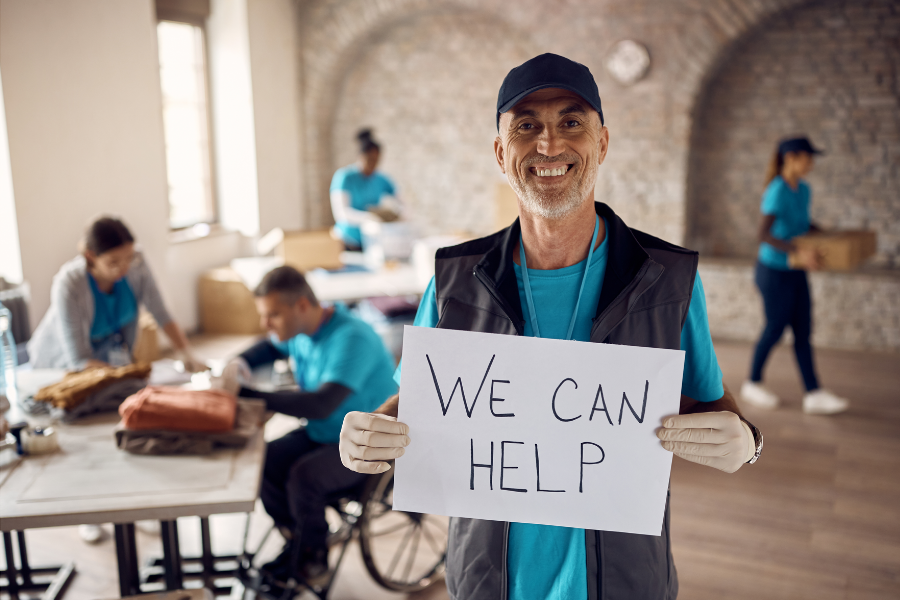 We Can Help — volunteer holding a hand-written help sign